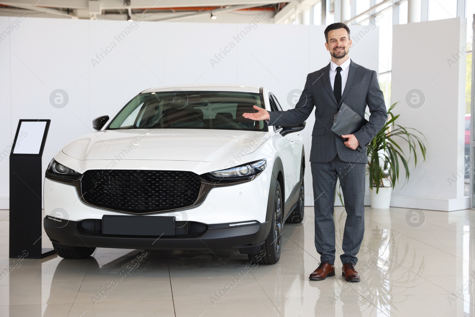 Photo of Smiling salesman with clipboard showing new car in salon