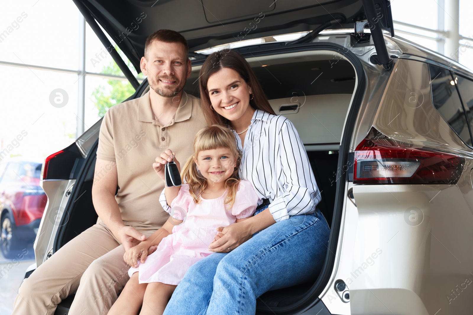Happy family with keys sitting in car trunk in salon Photo of Happy family with keys sitting in car trunk in salon