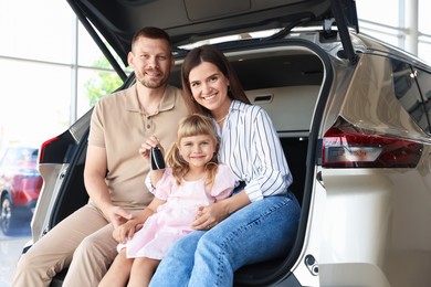 Photo of Happy family with keys sitting in car trunk in salon