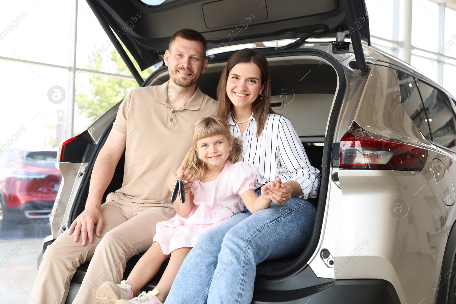 Photo of Happy family with keys sitting in car trunk in salon