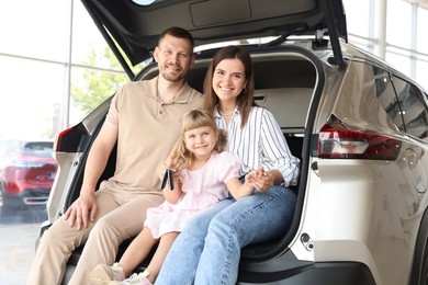 Photo of Happy family with keys sitting in car trunk in salon