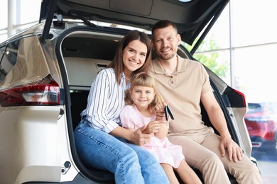 Photo of Happy family with keys sitting in car trunk in salon