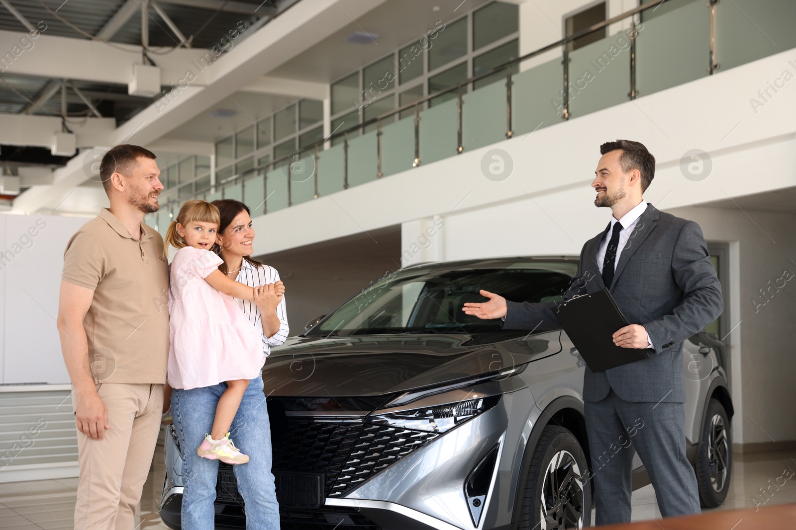 Photo of Salesman with clipboard showing new car to happy family in salon