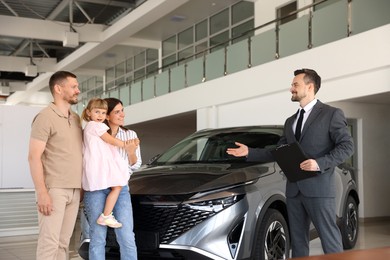 Photo of Salesman with clipboard showing new car to happy family in salon
