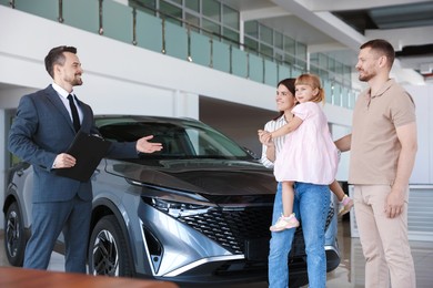 Photo of Salesman with clipboard showing new car to happy family in salon