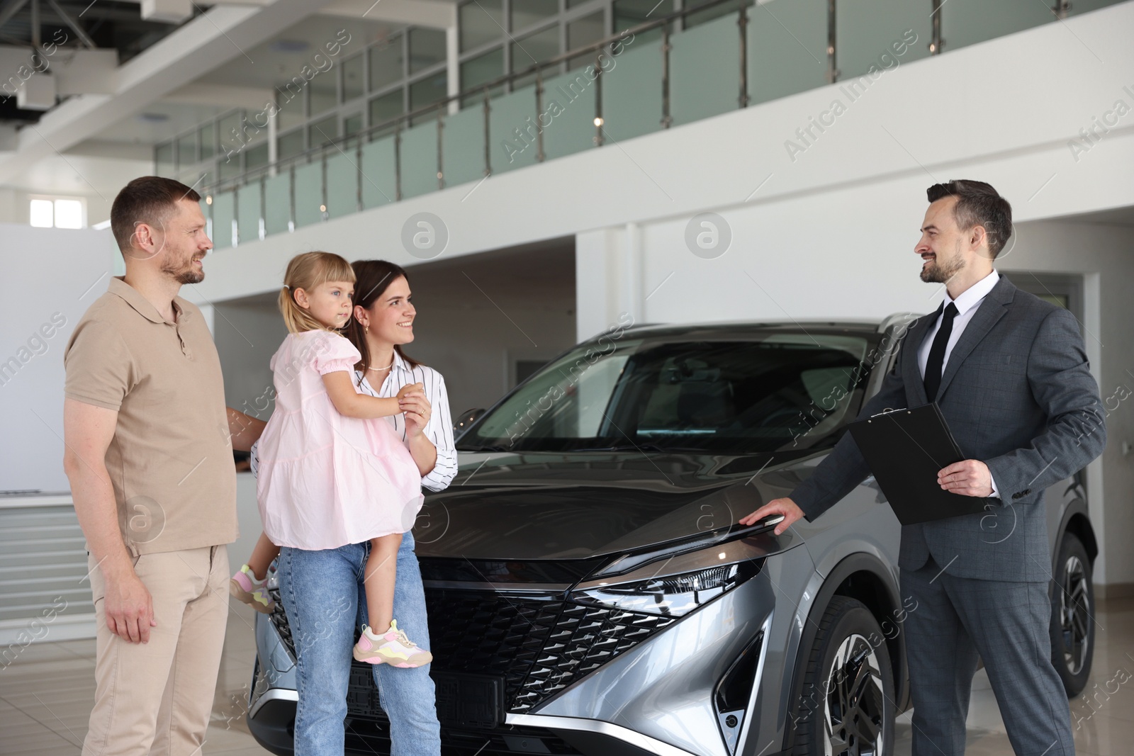 Photo of Salesman with clipboard showing new car to happy family in salon
