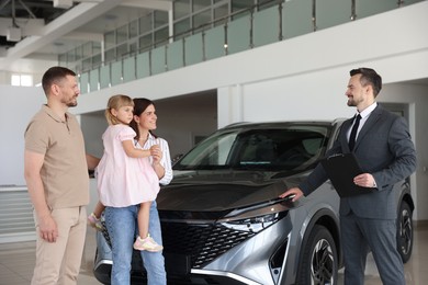 Photo of Salesman with clipboard showing new car to happy family in salon
