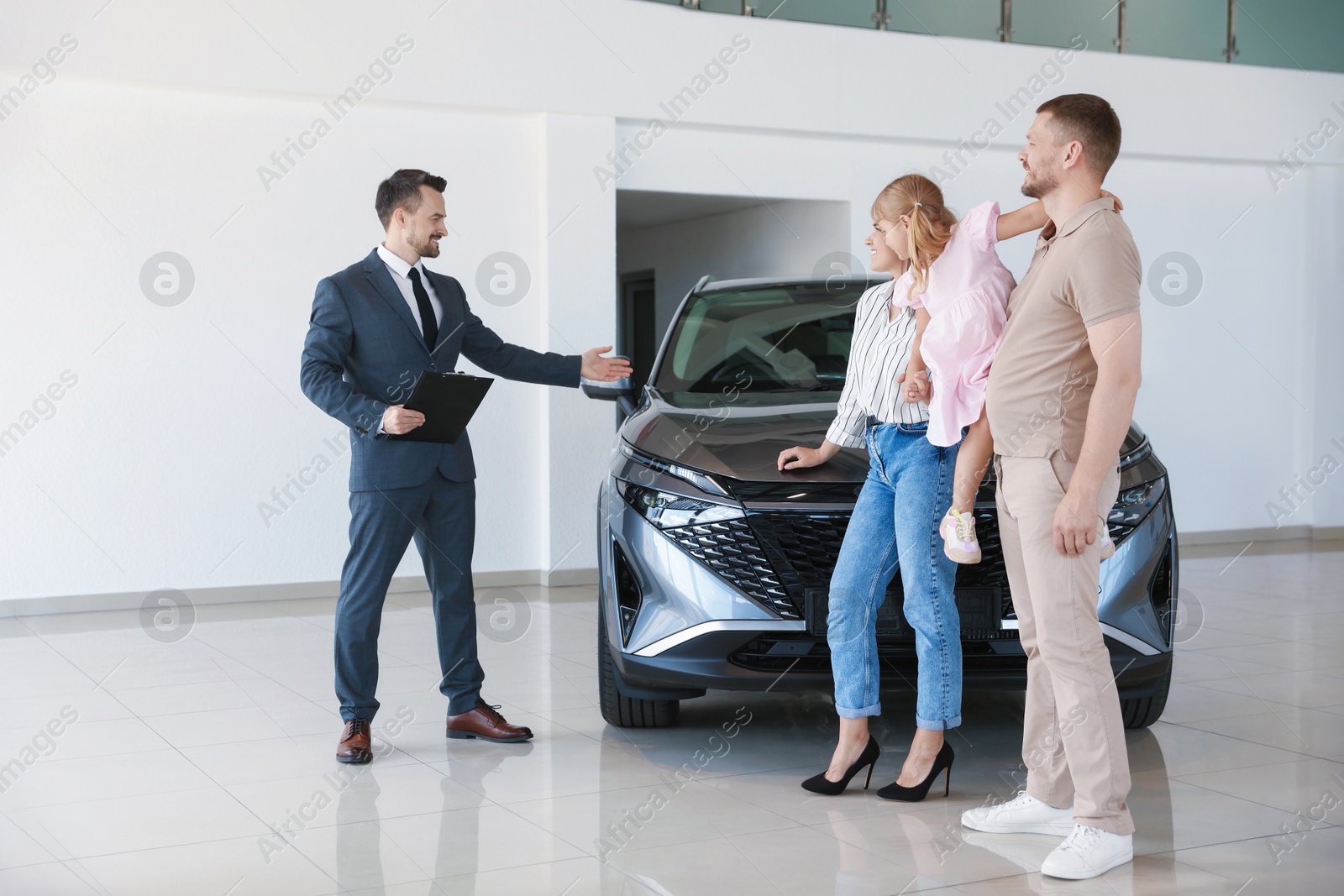 Salesman with clipboard showing new car to happy family in salon Photo of Salesman with clipboard showing new car to happy family in salon