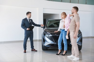 Photo of Salesman with clipboard showing new car to happy family in salon