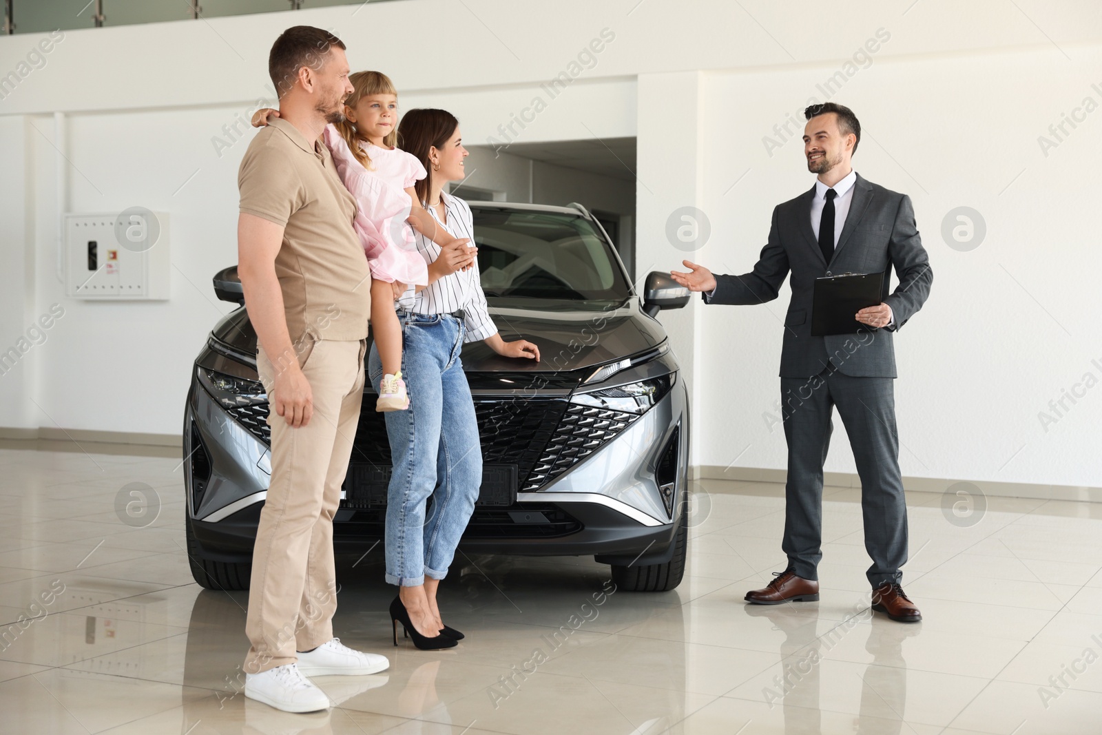 Salesman with clipboard showing new car to happy family in salon Photo of Salesman with clipboard showing new car to happy family in salon