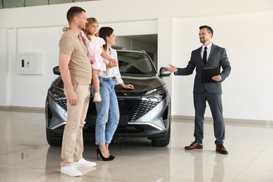 Photo of Salesman with clipboard showing new car to happy family in salon