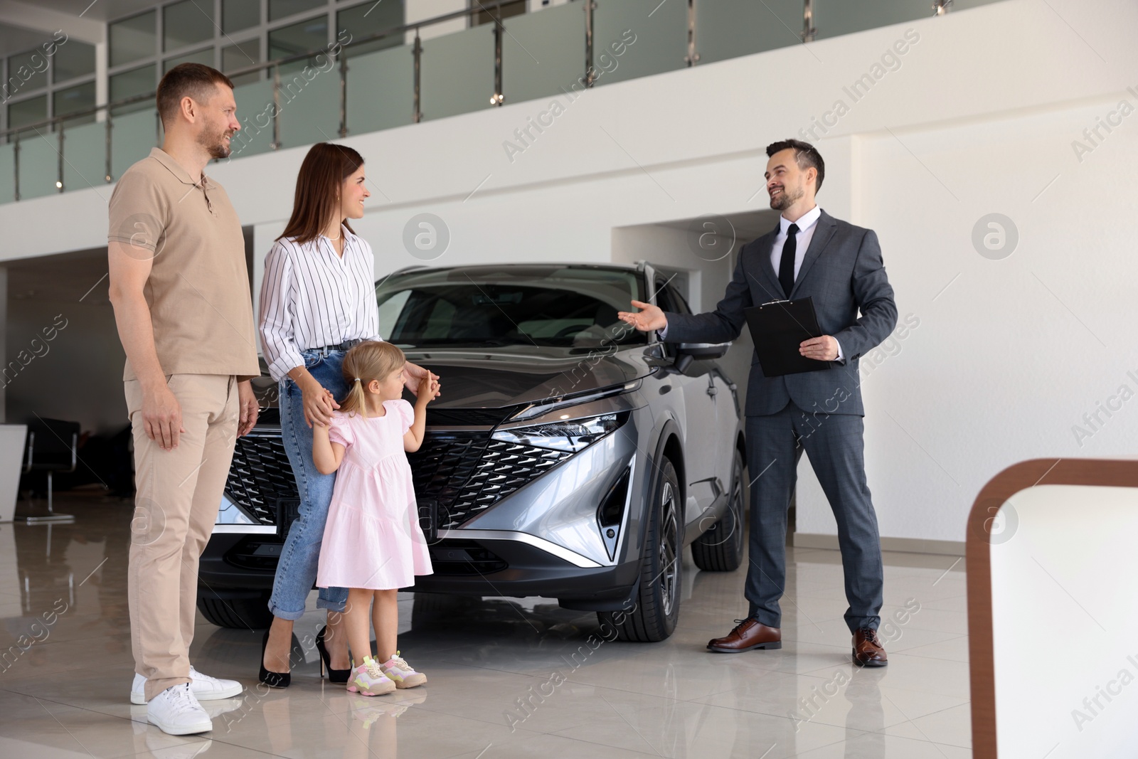 Photo of Salesman showing new car to happy family in salon, low angle view