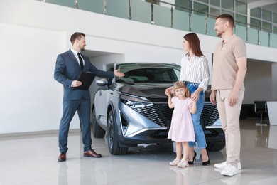 Photo of Salesman showing new car to happy family in salon, low angle view
