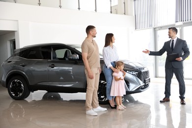 Photo of Salesman with clipboard showing new car to happy family in salon