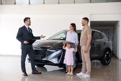 Photo of Salesman with clipboard showing new car to happy family in salon