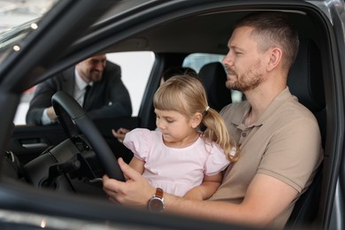 Photo of Family holding steering wheel inside new car and salesman, selective focus