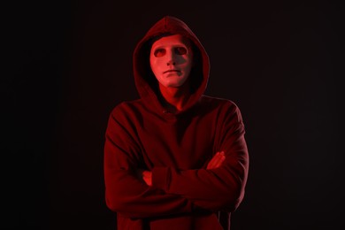Photo of Anonymity. Masked man on dark background with red light