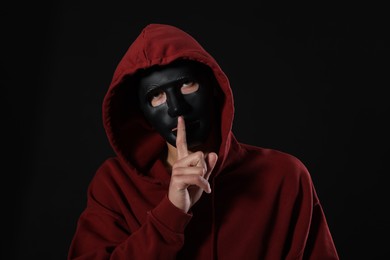 Photo of Anonymity. Man with mask showing hush gesture on dark background