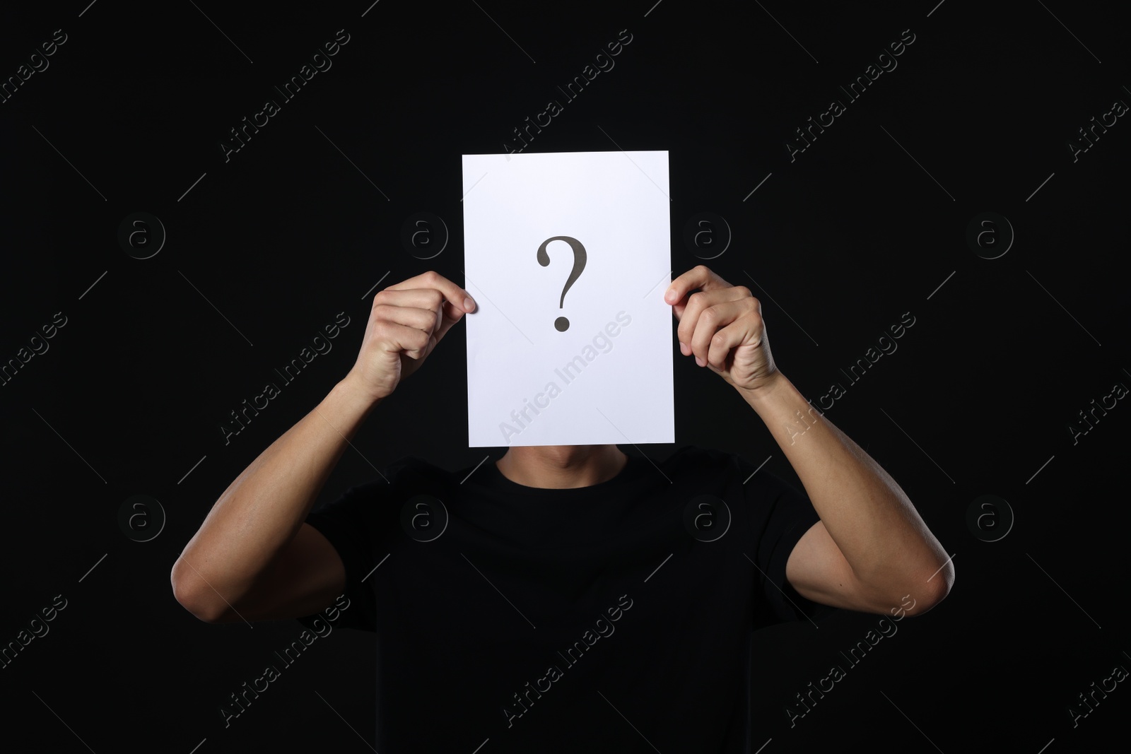 Photo of Man hiding behind paper sheet with question mark on dark background