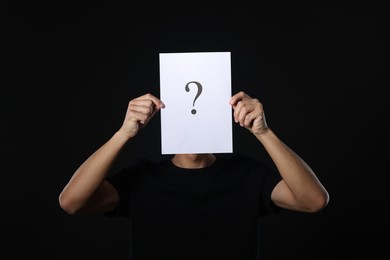 Photo of Man hiding behind paper sheet with question mark on dark background