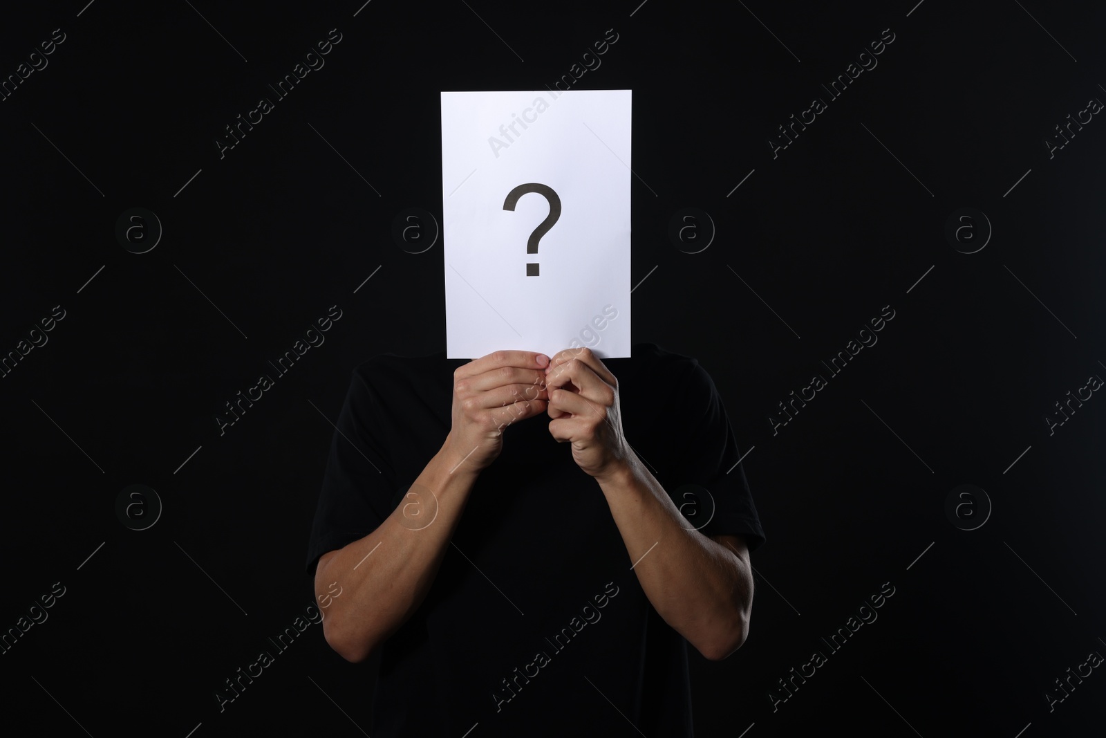 Photo of Man hiding behind paper sheet with question mark on dark background