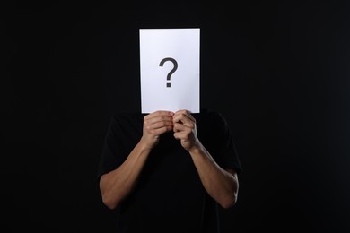 Photo of Man hiding behind paper sheet with question mark on dark background
