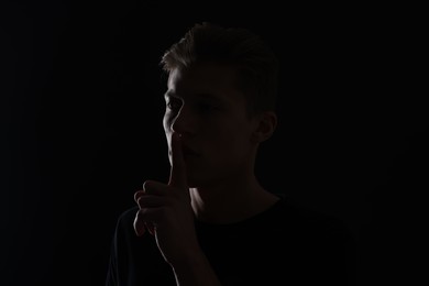 Photo of Anonymity. Man showing silence gesture in darkness