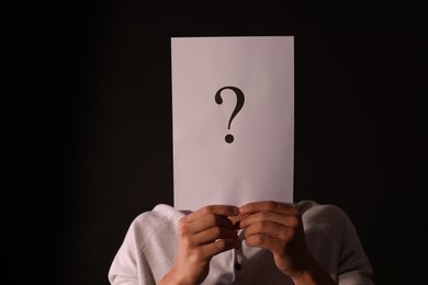 Photo of Man hiding behind paper sheet with question mark on dark background