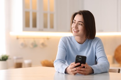 Photo of Woman using modern smartphone at table in kitchen. Space for text