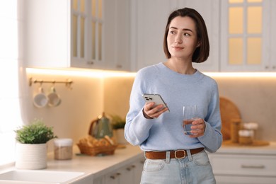 Photo of Woman with glass of water using modern smartphone in kitchen. Space for text