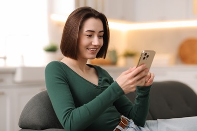 Photo of Woman using modern smartphone on sofa at home