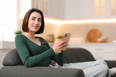 Photo of Woman using modern smartphone on sofa at home. Space for text