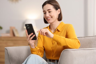 Photo of Woman using modern smartphone in armchair at home