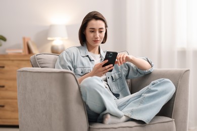 Photo of Woman using modern smartphone in armchair at home