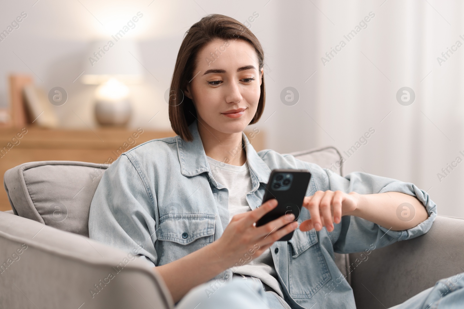 Photo of Woman using modern smartphone in armchair at home