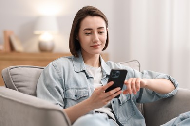 Photo of Woman using modern smartphone in armchair at home