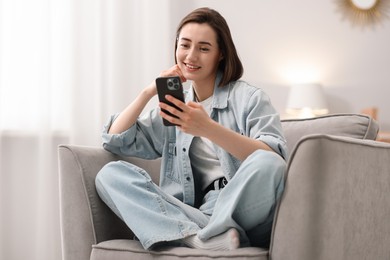 Photo of Woman using modern smartphone in armchair at home