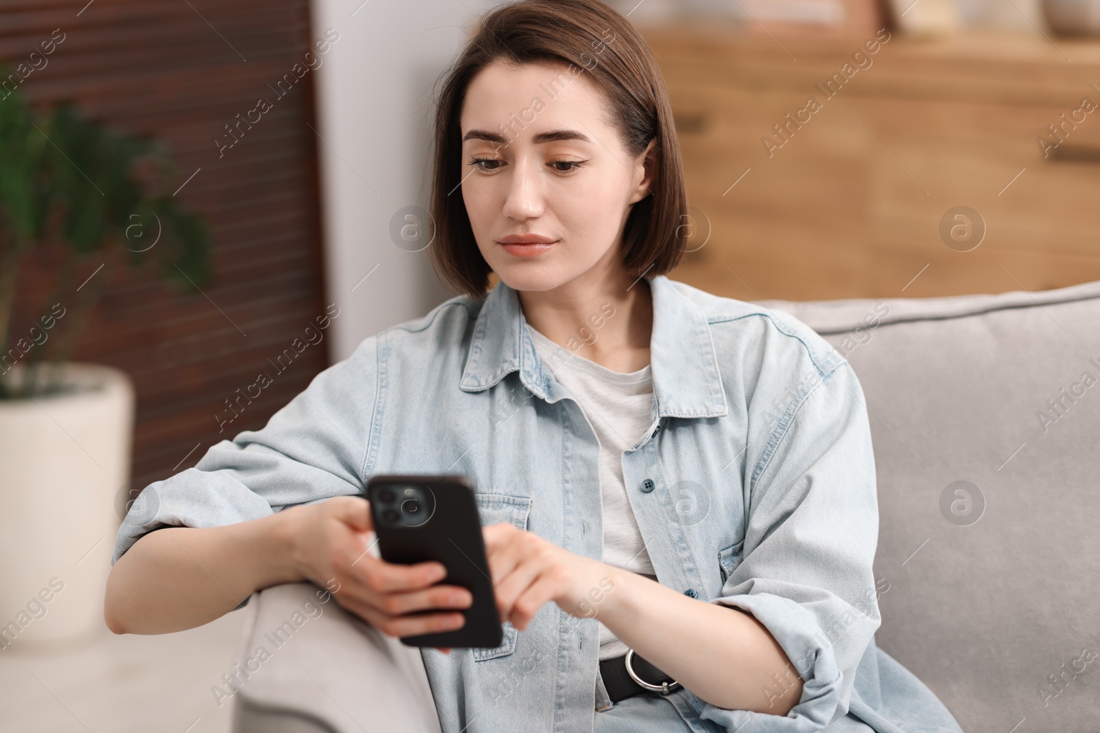 Photo of Woman using modern smartphone in armchair at home