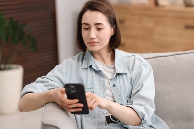 Photo of Woman using modern smartphone in armchair at home
