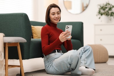 Photo of Woman using modern smartphone on floor at home