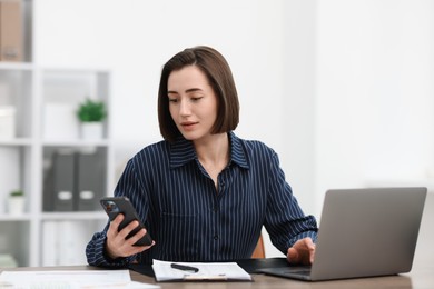 Photo of Beautiful woman using her smartphone while working at desk in office