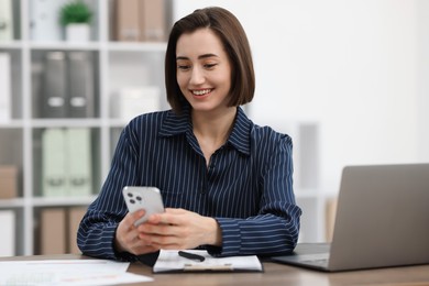 Photo of Beautiful woman using her smartphone while working at desk in office