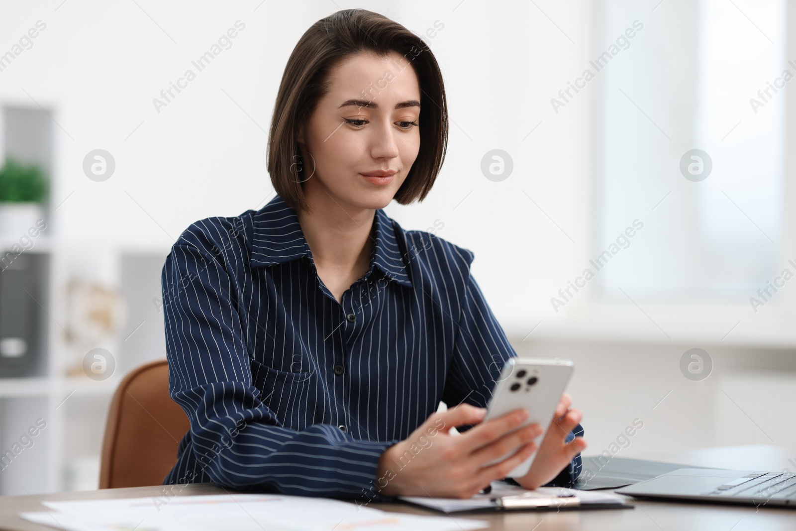 Photo of Beautiful woman using her smartphone while working at desk in office