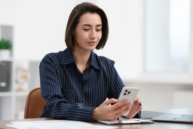 Photo of Beautiful woman using her smartphone while working at desk in office