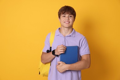 Photo of Smiling teenage boy with book and backpack on yellow background