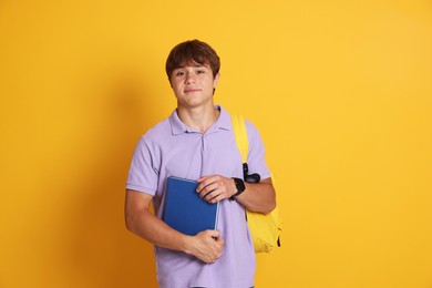 Photo of Cute teenage boy with book and backpack on yellow background