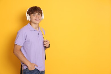Photo of Smiling teenage boy with headphones on yellow background. Space for text