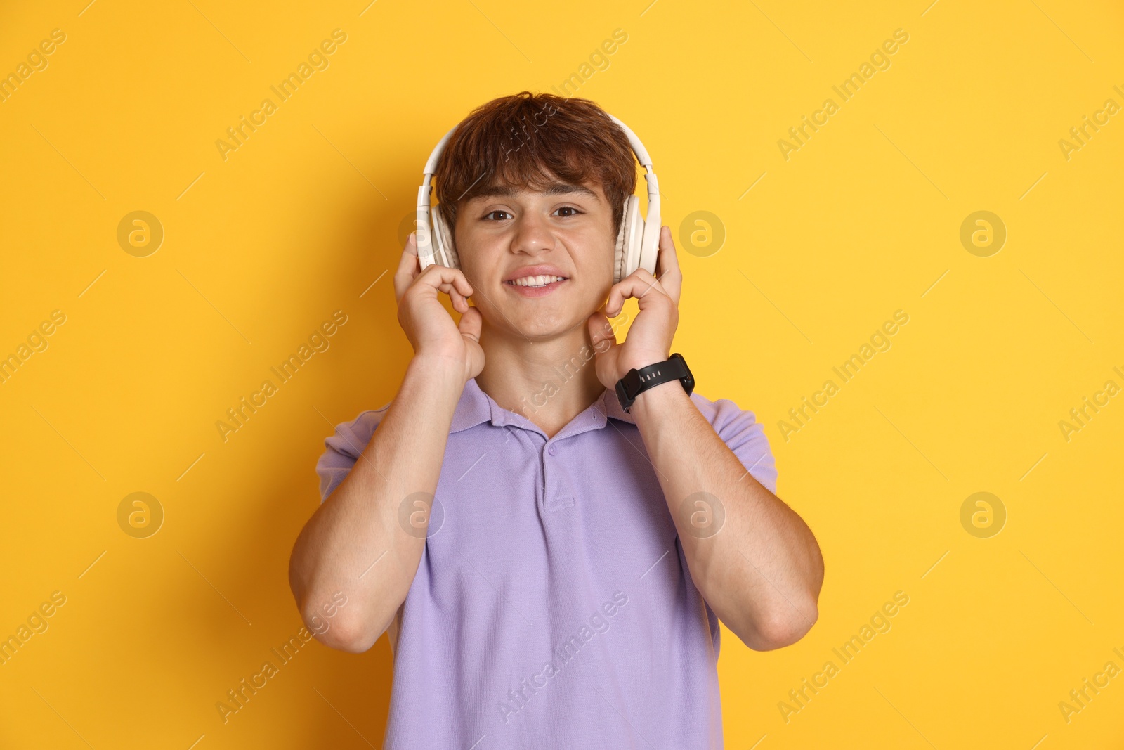 Photo of Smiling teenage boy listening to music on yellow background