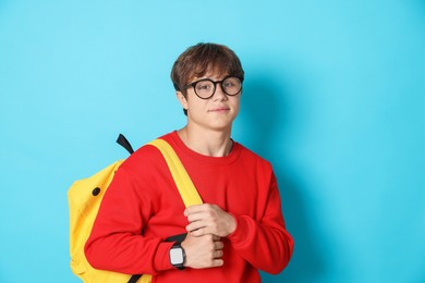 Photo of Cute teenage boy in glasses with book and backpack on light blue background