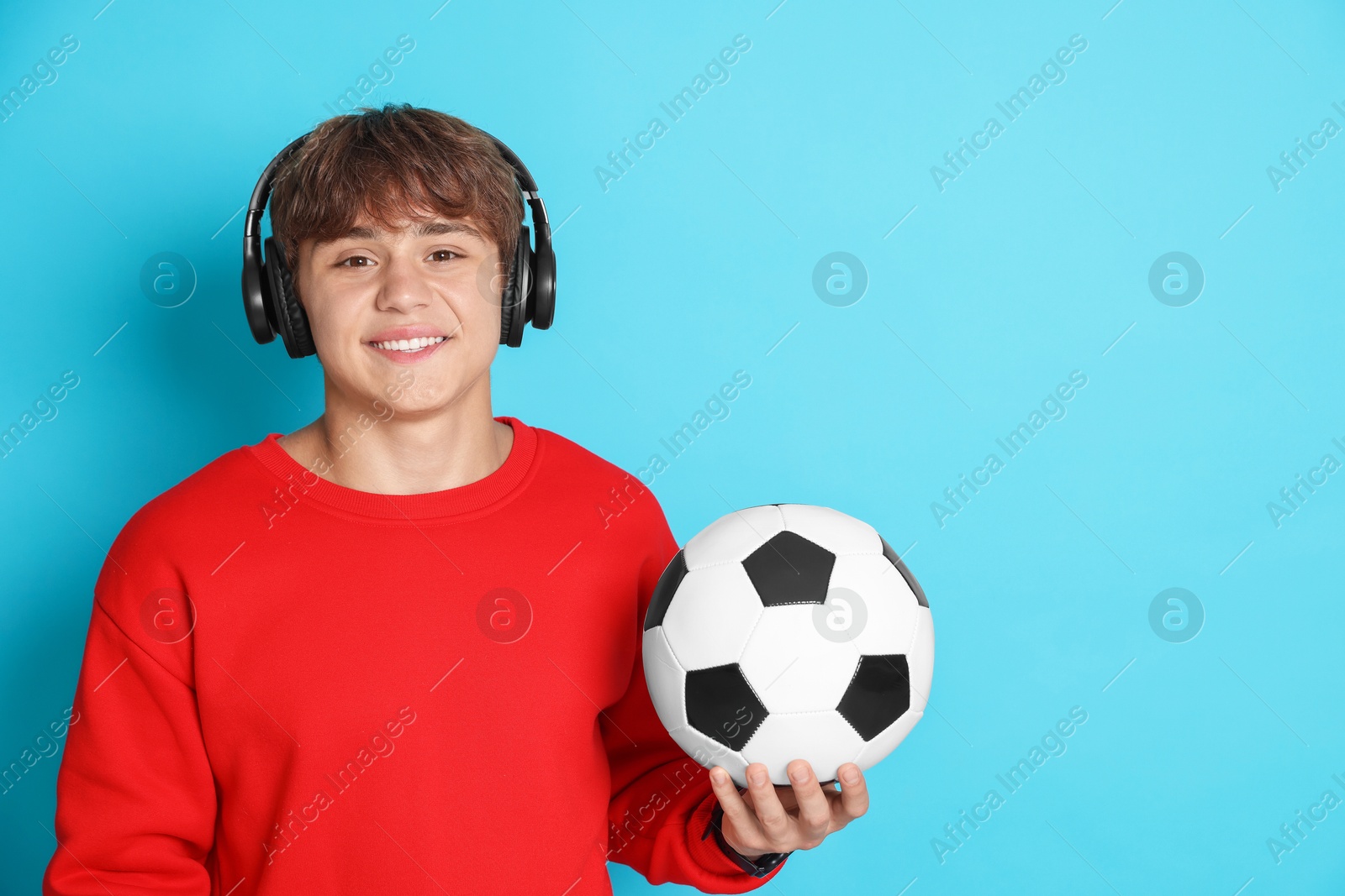 Photo of Portrait of smiling teenage boy in headphones with soccer ball on light blue background. Space for text